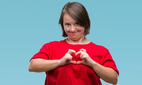 A young woman with Down’s syndrome makes the shape of a heart
