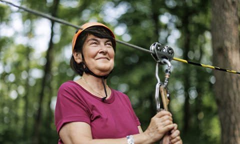 Taking part in riskier activities: an older woman prepares to go on a zip line in the woods
