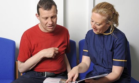 A nurse uses a book with pictures to help explain a medical intervention to a person with a learning disability