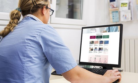 A female nurse in uniform sits at a desk at work using a computer, with the new RCNi Learning platform on screen