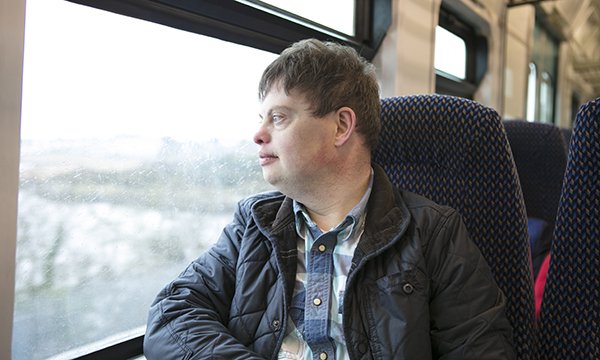 Image of a man with Down’s syndrome looking out of a train window. Clare Taylor of mental health and learning disability at the charity Turning Point, talks about how to fix the system of care for people with learning disabilities and autism.
