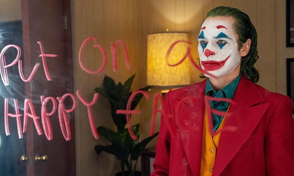 Picture shows a scene from the movie Joker in which the star, Joaquin Phoenix, wearing clown makeup, is looking at a mirror on which has been written, ‘Put on a happy face.’ The article argues that Joker’s portrayal of mental illness is worrying. 