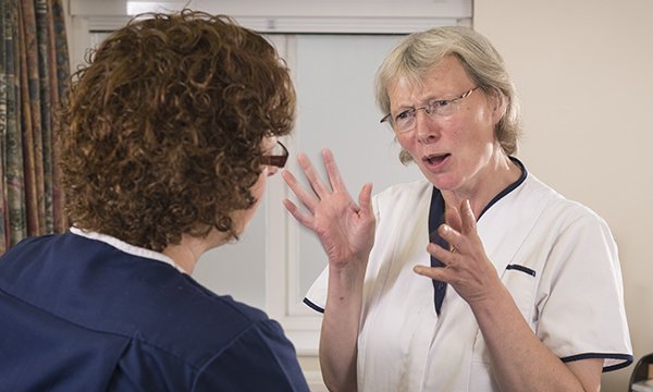 two nurses talking – one is gesticulating and looking angry