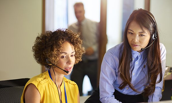 Picture shows two women wearing headsets, and one of them is speaking to a caller. Nurse specialists at Prostate Cancer UK receive detailed training including mentors and a learning contract to equip them to deal with requests for help and advice.
