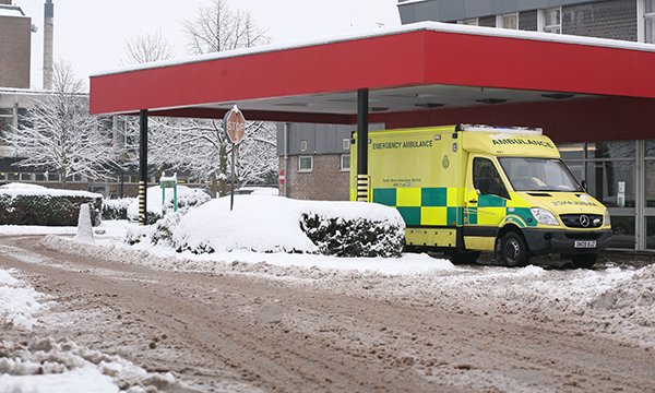 Image shows ambulance outside hospital emergency department in winter in the snow