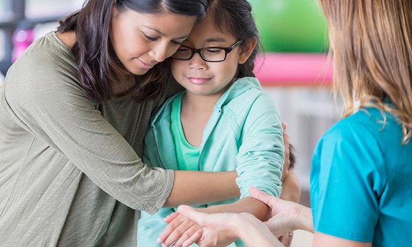 Picture shows a woman comforting a young girl while a nurse holds her arm