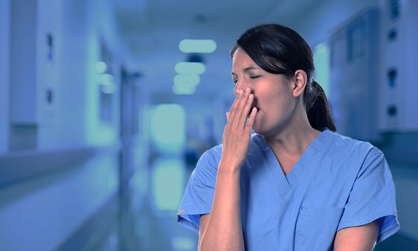 A young nurse hold a hand to her mouth while yawning