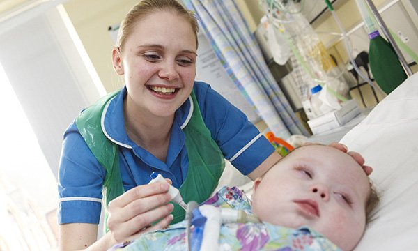 A young nurse smiles as she leans over a baby lying in a hospital bed – more than a century after the first children’s nurse was registered, senior figures in the specialty fear that progress made over the years has now stalled