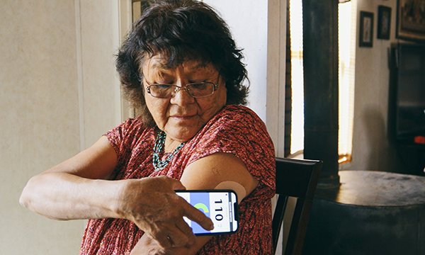 An older woman uses a diabetes app to measure blood sugars on her phone by placing it on a patch on her upper arm