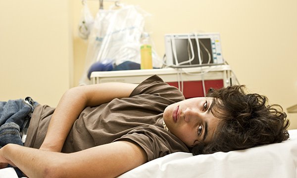 A young person lying on a hospital bed with a melancholy expression: many young adults can fall between the gaps of paediatric and adult emergency services