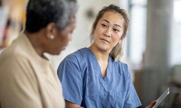 A nurse in blue scrubs discusses side effects with a cancer patient