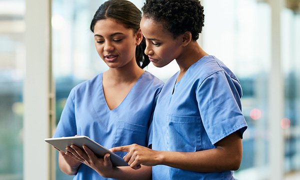 Two nurses look at a hand-held tablet screen together while working on a ward