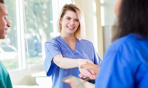 A nurse in blue scrubs shakes the hand of her new employer, after registering with the NMC