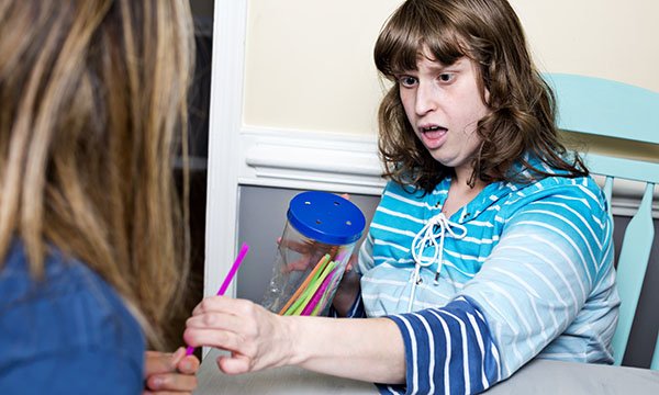 A young woman with learning disabilities interacting with a healthcare professional while holding a jar of multicoloured straws