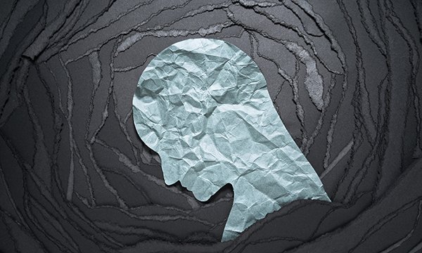 Silhouette of a head looking down cut from a sheet of green crumpled paper on a black background indicating mental health and well-being