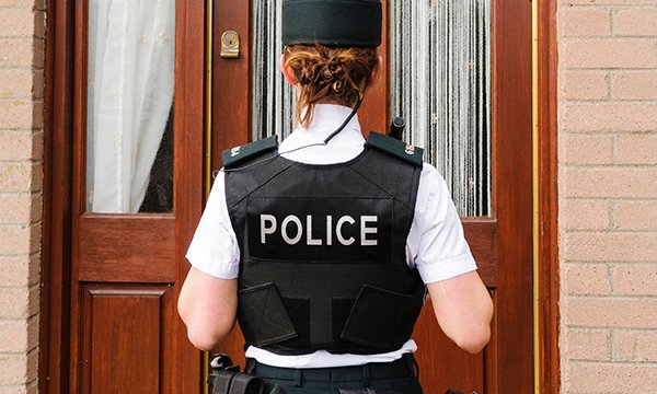 A uniformed police officer standing outside a front door