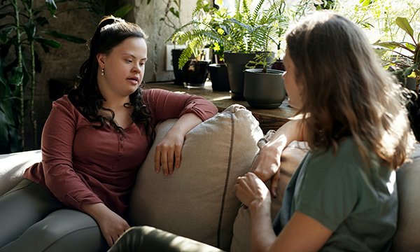 Two women, one of whom has a learning disability, sit on a sofa talking to each other