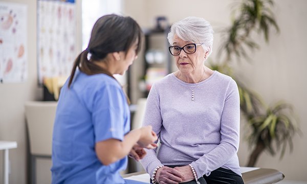 A nurse talks to an older woman who has a serious expression on her face