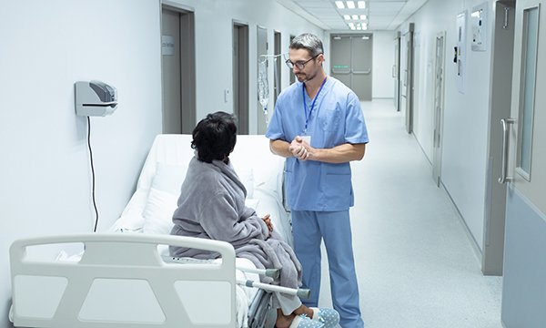 A medic talks to a patient sitting on a bed in a ward corridor