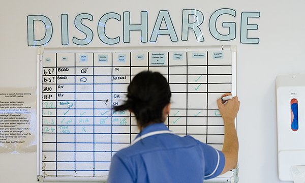 A nurse writes in a grid on a hospital white board with the word 'discharge' in capital letters above it