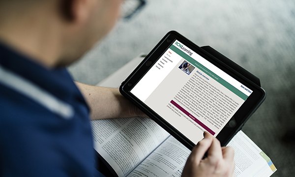 Nurse holds nursing journal and tablet computer to read an RCNi Learning module, which will help them fulfil their CPD requirements for revalidation