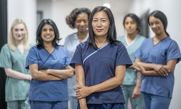 A nurse stands in front of a line of other nurses, looking happy and confident. Yet nurses often downplay their role