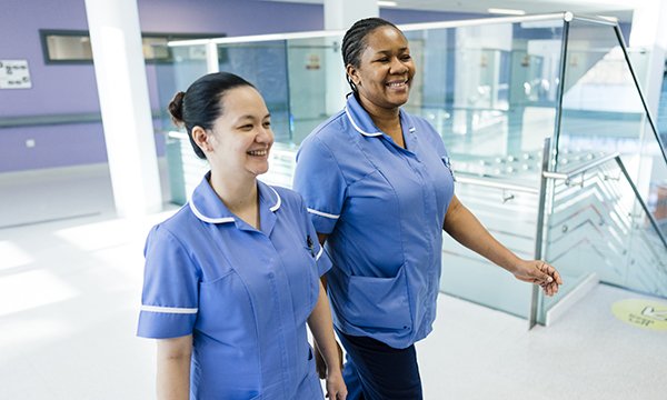 Two nurses happily walk through hospital lobby. Study founds consitency in nurse rostering is good for staff morale