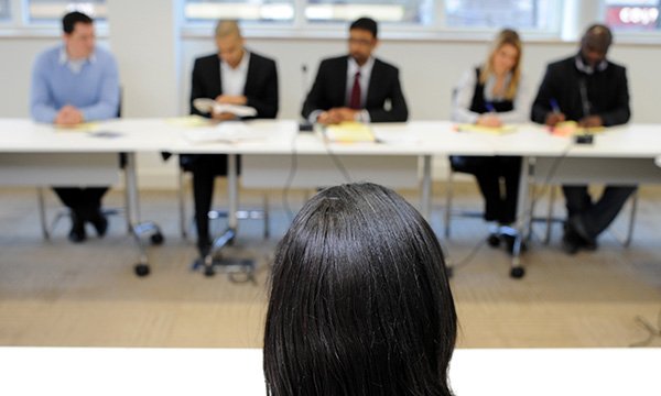 Woman, whose head is seen from behind, faces an official panel of questioners. NMC's independent panels will investigate cases of suspended registration fraud
