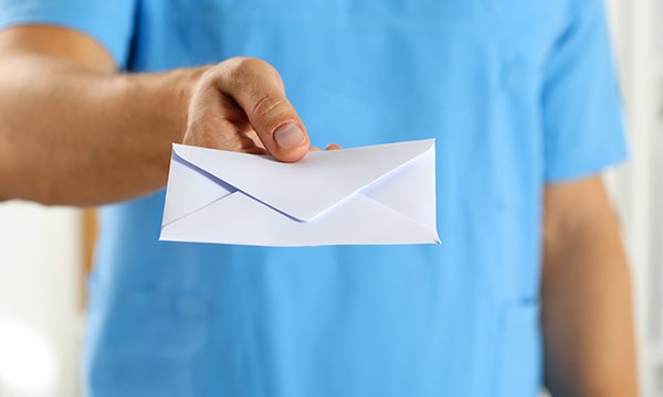 A nurse’s hand holding and offering a white envelope containing a letter of resignation