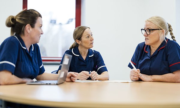 Three nursing colleagues sit together in a debrief session, which can be effective in managing workplace trauma