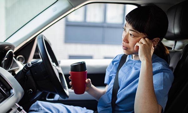 Community nurse looks fed up as she sips hot drink in her car between home visits. Many community nurses are seeing a delay in payment of part of their 2022-23 pay deal