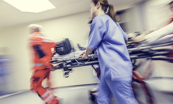 A fast-paced image of paramedics and nursing staff swiftly rushing a patient on a trolley into the emergency department