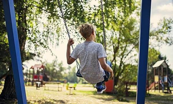 A young boy sitting on a swing in a children’s play area in a park