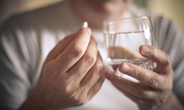 Close up of someone preparing to take a pill with a glass of water