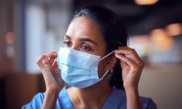Photo of a nurse securing a face mask behind her ear: withdrawing face mask recommendation for hospitals and other health and care settings in Scotland has been described as dangerous for staff
